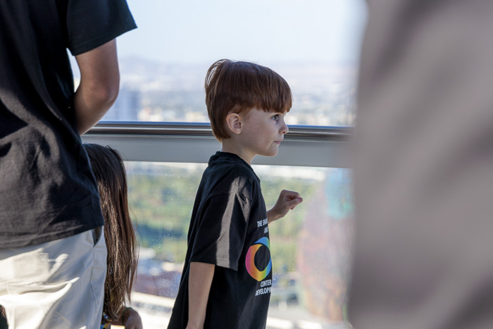 A young boy, standing with his family, looks out the window of an observation wheel at the city